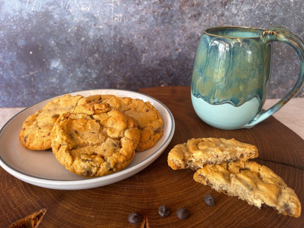 a plate of cookies with a teal coloured mug to the right. they are sitting on a slab of wood.